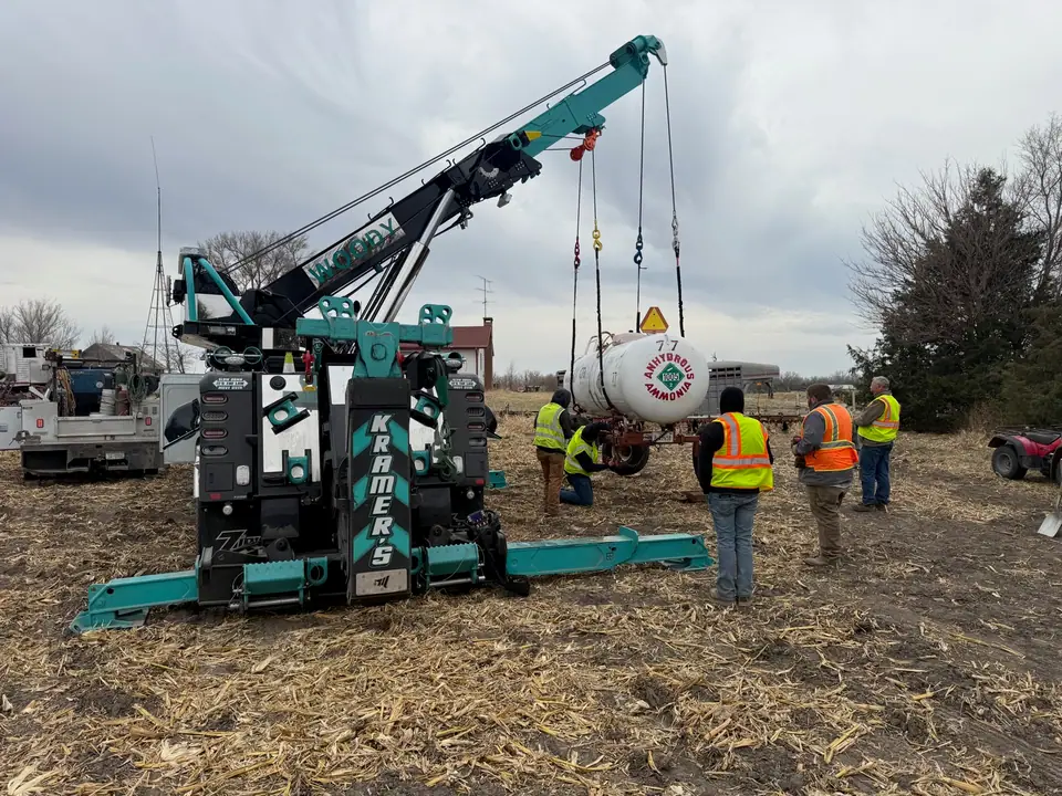 Kramer's teal rotator lifting a tank at a recovery scene while the crew works